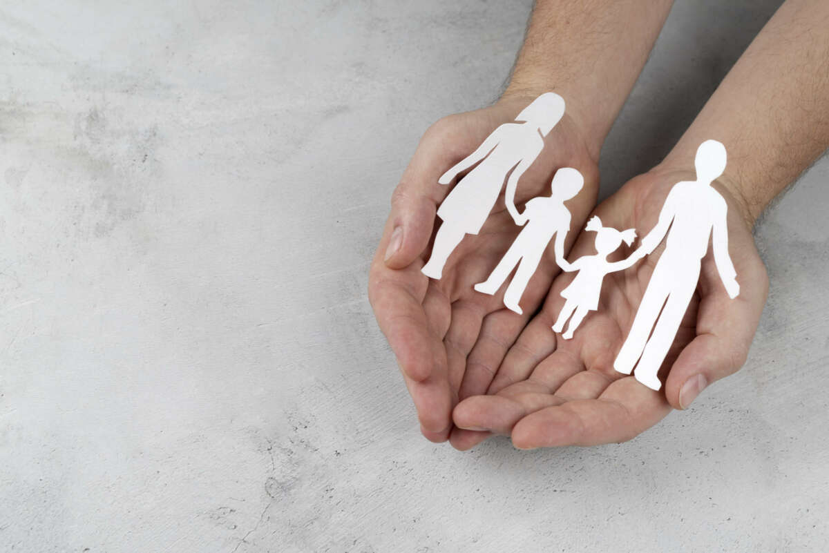 Dos manos sosteniendo un recorte de papel con la forma de una familia. 