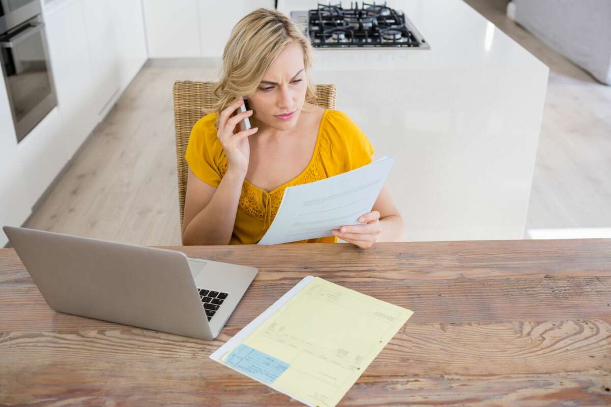 Una mujer realiza una reclamación por teléfono mientras observa unos papeles. Foto: Freepik.