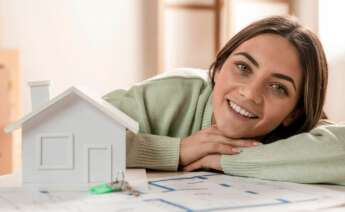 Una joven recostada en sus manos con una maqueta y los planos de una casa. Foto: Freepik.