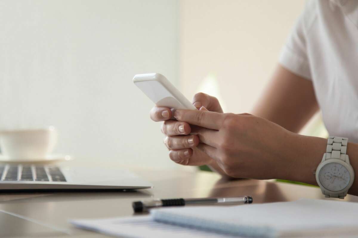 Una persona consulta el teléfono móvil mientras realiza un trámite con el ordenador. Foto: Freepik.