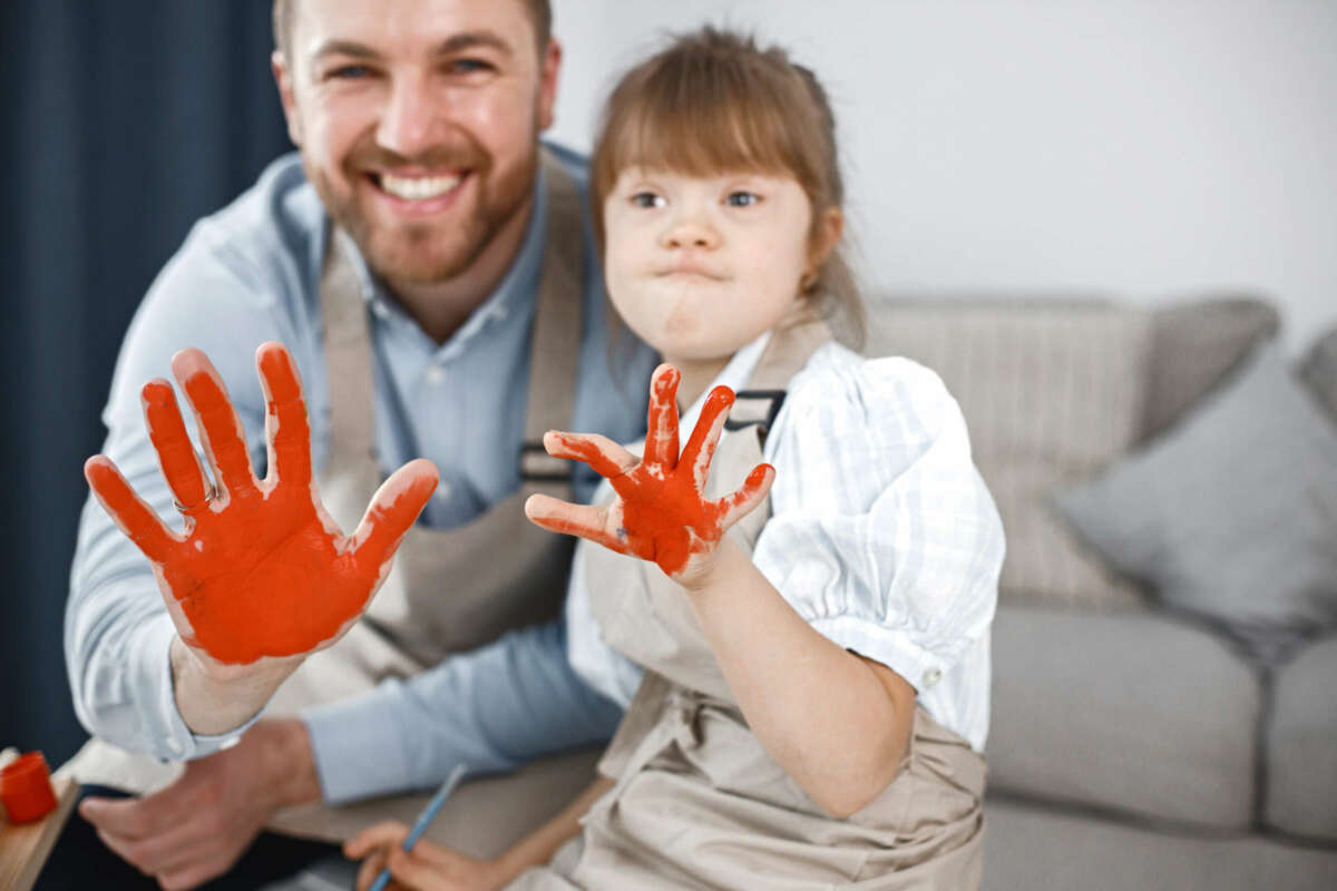 Padre e hija con las manos pintadas de naranja. 