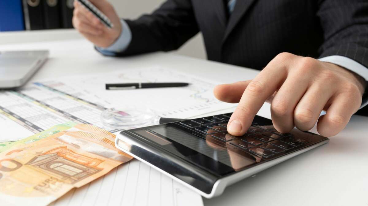 Un hombre realiza cálculo mediante una calculadora, en un escritorio en el que hay un billete de 50 euros y algunos papeles. Foto: Freepik.
