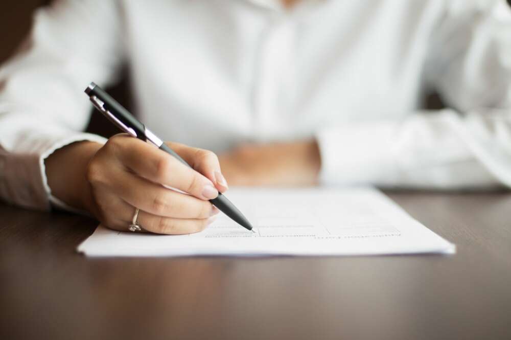 Una mujer firma un documento en un despacho. Foto: Freepik.