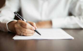 Una mujer firma un documento en un despacho. Foto: Freepik.