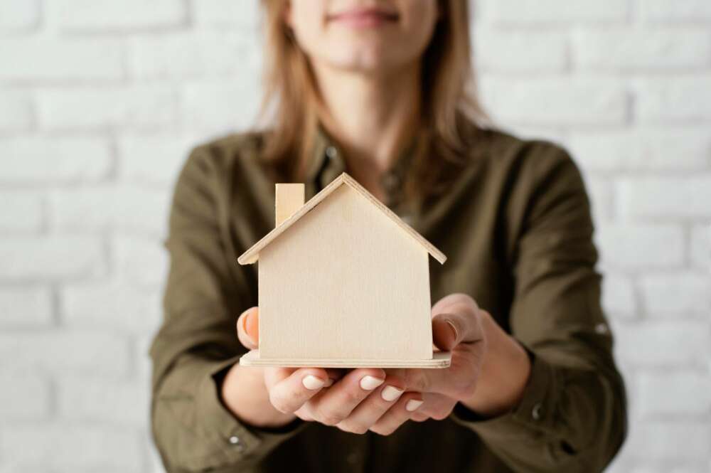 Una mujer sostiene una estructura con forma de casa hecha de madera. Foto: Freepik.