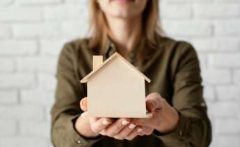 Una mujer sostiene una estructura con forma de casa hecha de madera. Foto: Freepik.