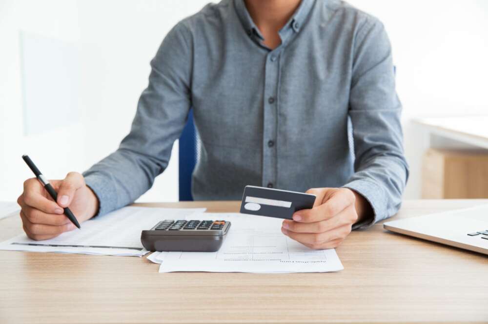 Una persona utiliza una calculadora y una tarjeta bancaria. Foto: Freepik.