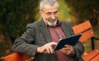 Hombre mayor leyendo en su tablet en la banca de un parque.