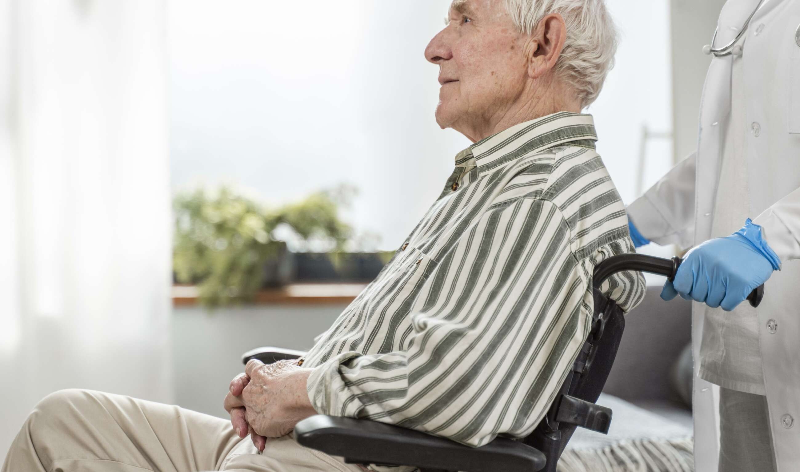 Adulto mayor sentado en una silla de ruedas con asistencia