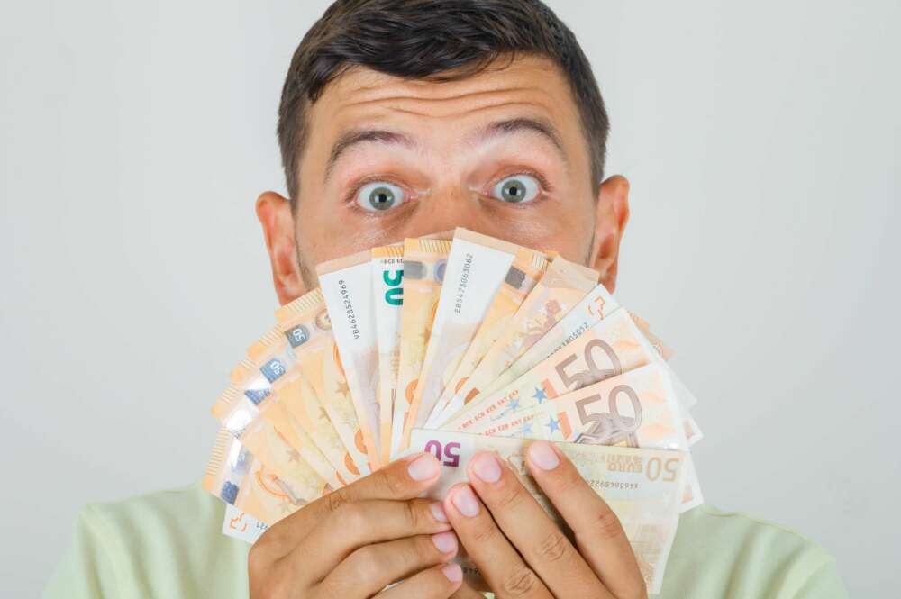 Un hombre sostiene un abanico de billetes de 50 euros tras solicitar un microcrédito. Foto: Freepik.