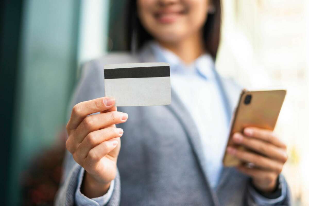 Un mujer sostiene una tarjeta bancaria mientras consulta su móvil. Foto: Freepik.