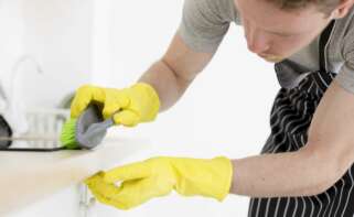 trabajador del hogar limpiando con guantes la esquina de un mueble