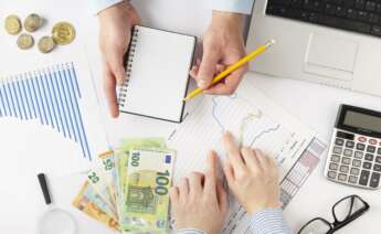 Dos personas sacando cuentas sobre un escritorio, con euros en billetes y gráficos