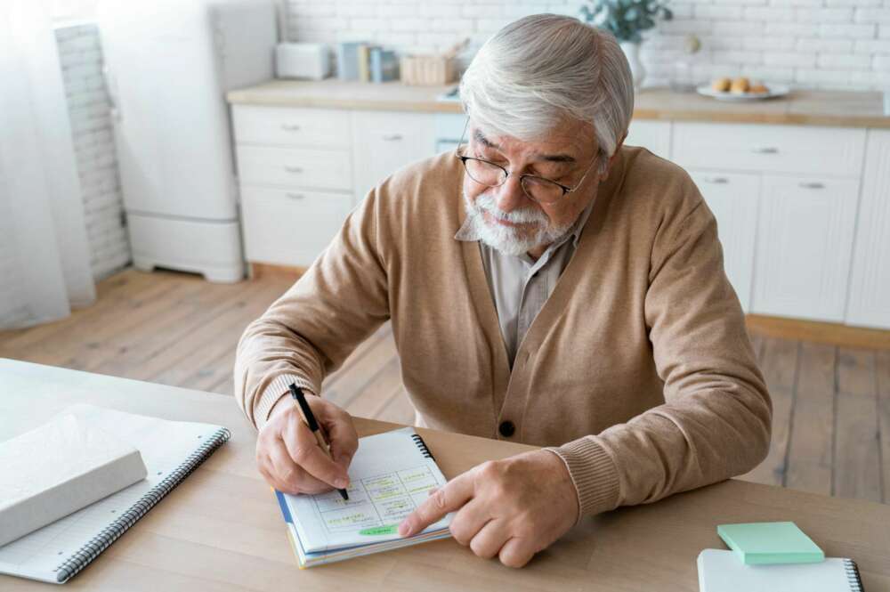 Un beneficiario de una pensión de jubilación hace unas anotaciones en una libreta. Foto: Freepik,