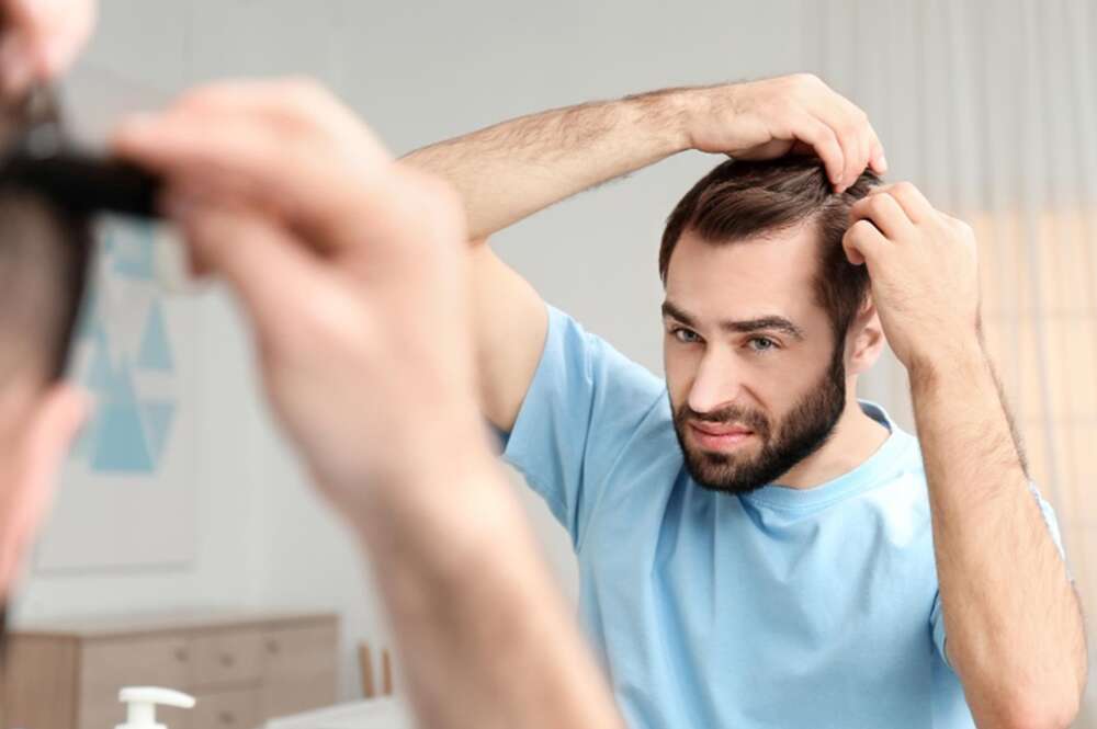Un hombre observa su cabello frente al espejo