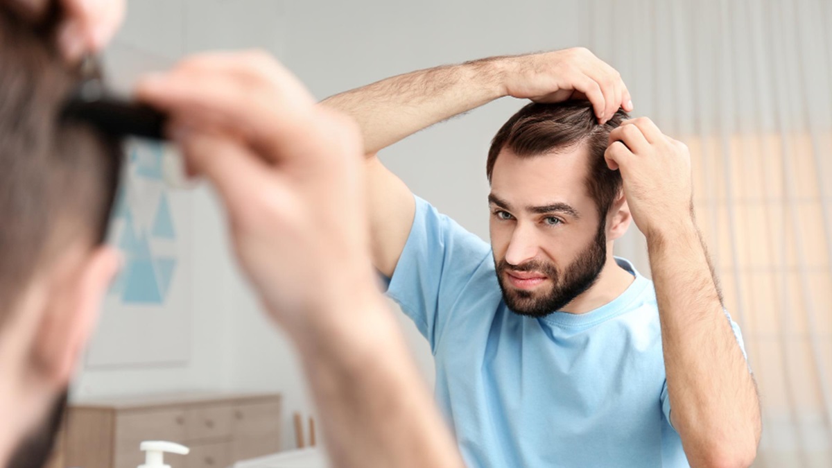 Un hombre observa su cabello frente al espejo