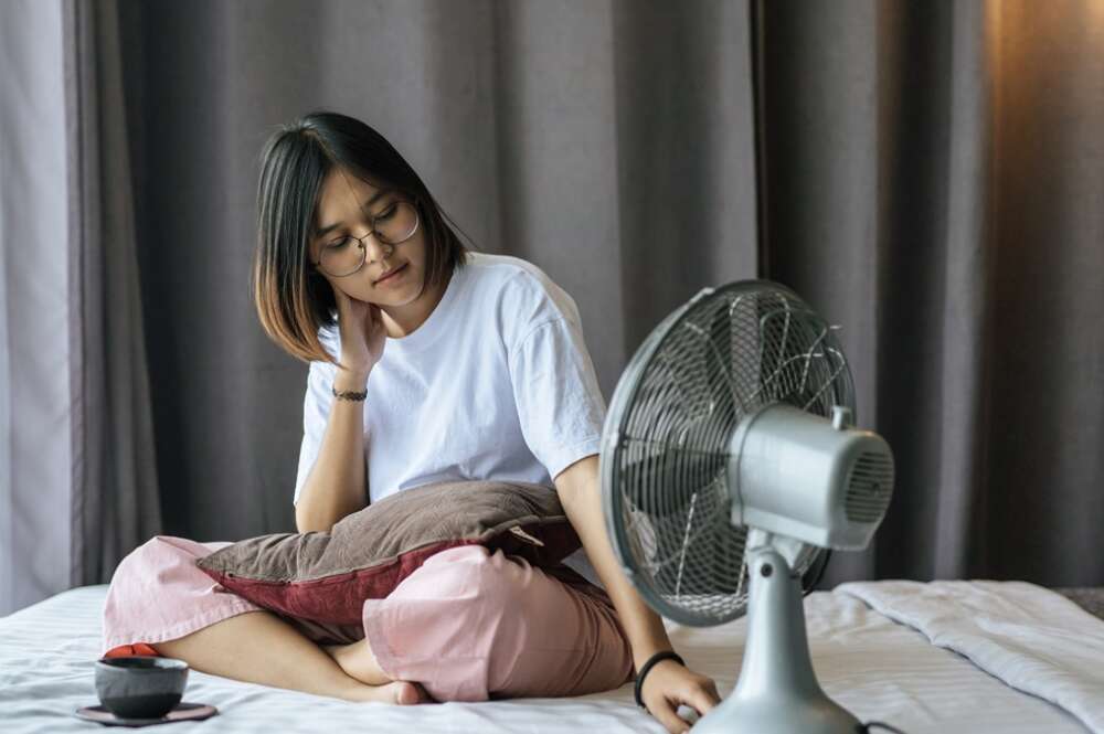 Una chica en su dormitorio con un ventilador