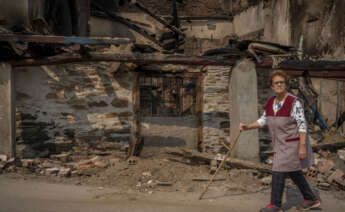 Una vecina pasea junto a una vivienda calcinada tras el incendio forestal acontecido en el pueblo de Alixo (O Barco de Valdeorras), en Ourense / Brais Lorenzo (EFE)