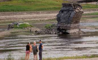 Tres personas junto al río Miño, cuyo bajo caudal ha dejado a la vista las ruinas del antiguo Portomarín, que en los años 60 del siglo pasado fue anegado por el embalse de Belesar