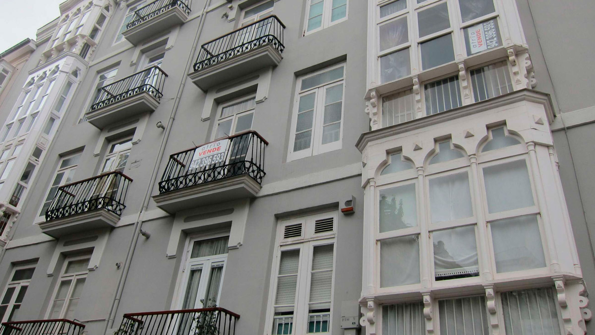 Imagen de la fachada de un edificio con un cartel de "se vende" en uno de los pisos