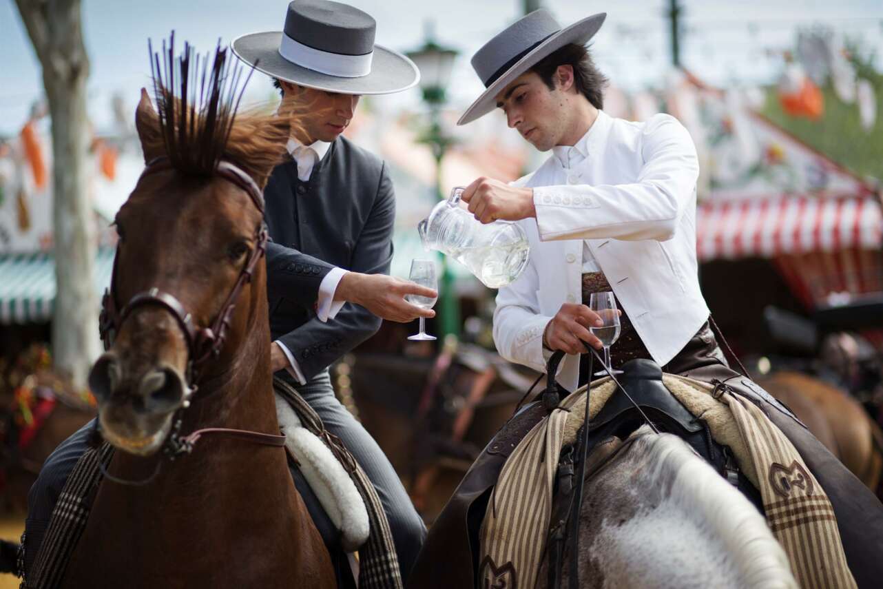 Dos personas a caballo bebiendo rebujito
